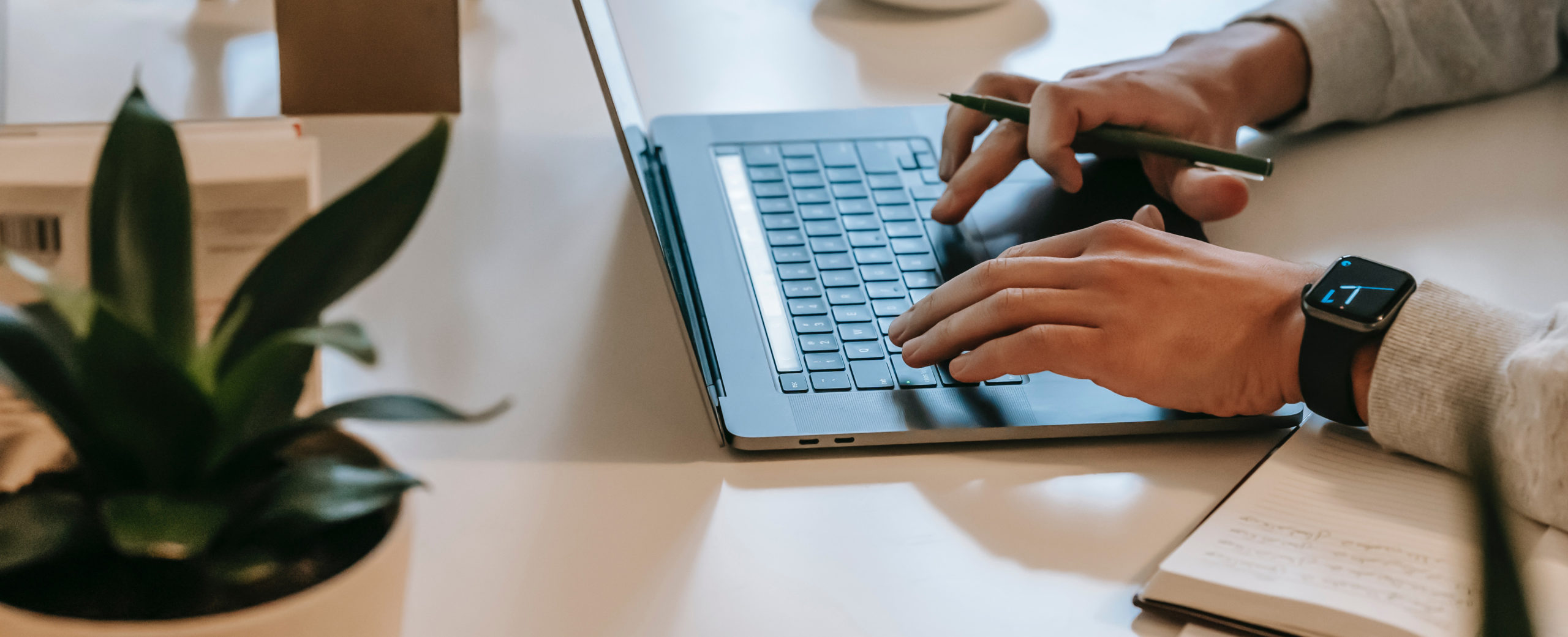 person typing on laptop with a pen writing things down